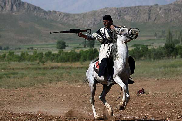 مردی با لباس بختیاری سوار براسب سفید درحال تیراندازی 